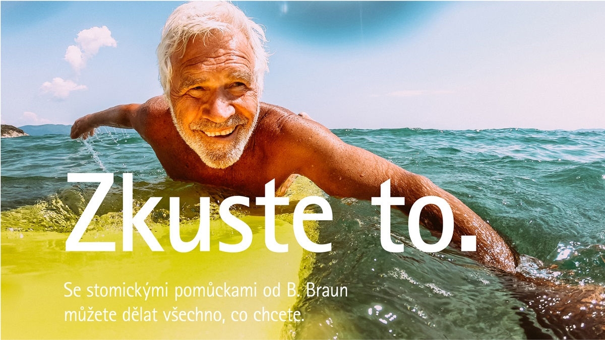 Starší muž s bílými vlasy leží na žlutém surfařském prkně a vesluje v oceánu pod čistou modrou oblohou.