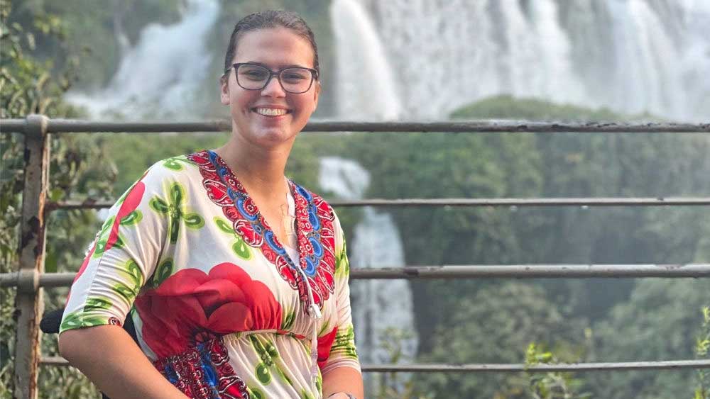Usmívající se dívka sedí na invalidním vozíku před vodopádem.