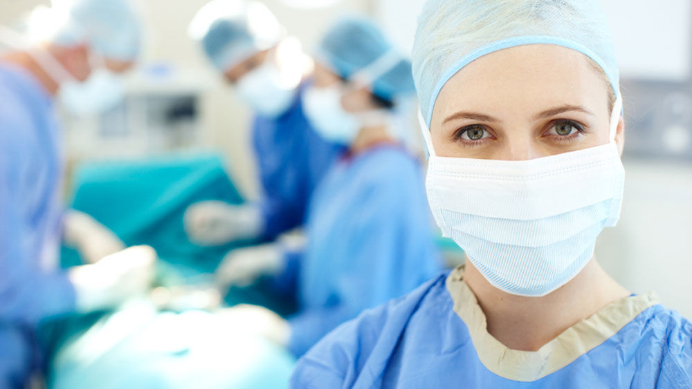 V popředí je chirurgyně, v pozadí jsou tři další chirurgové během operace