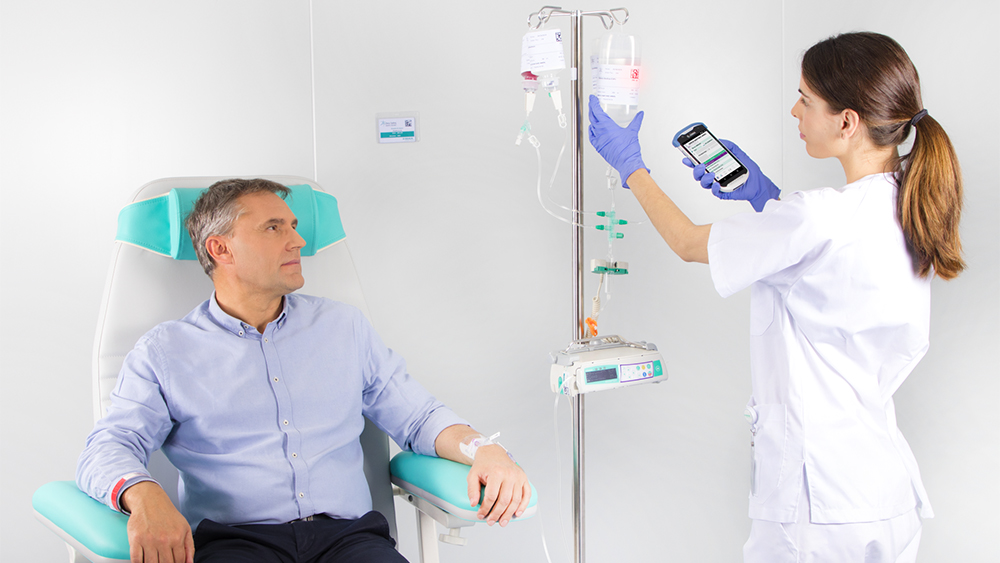 Na obrázku je pacient sedící v křesle, který dostává infuzi z infuzní pumpy B. Braun, zatímco sestra nastavuje dávkování infuze na zařízení.