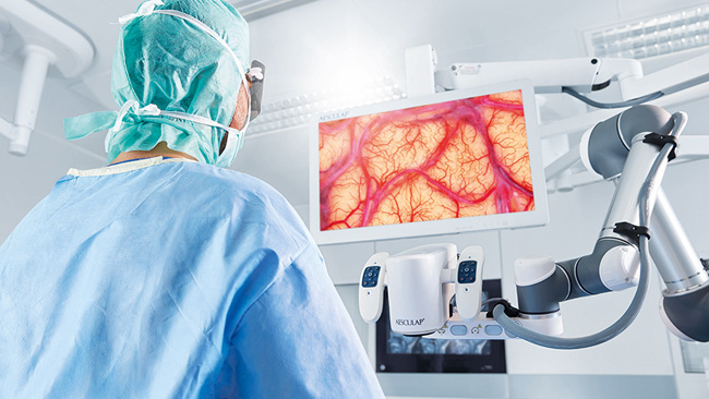 Chirurg provádí neurochirurgický zákrok pomocí Aesculap Aeos®, přičemž stojí vzpřímeně a dívá se na monitor. 