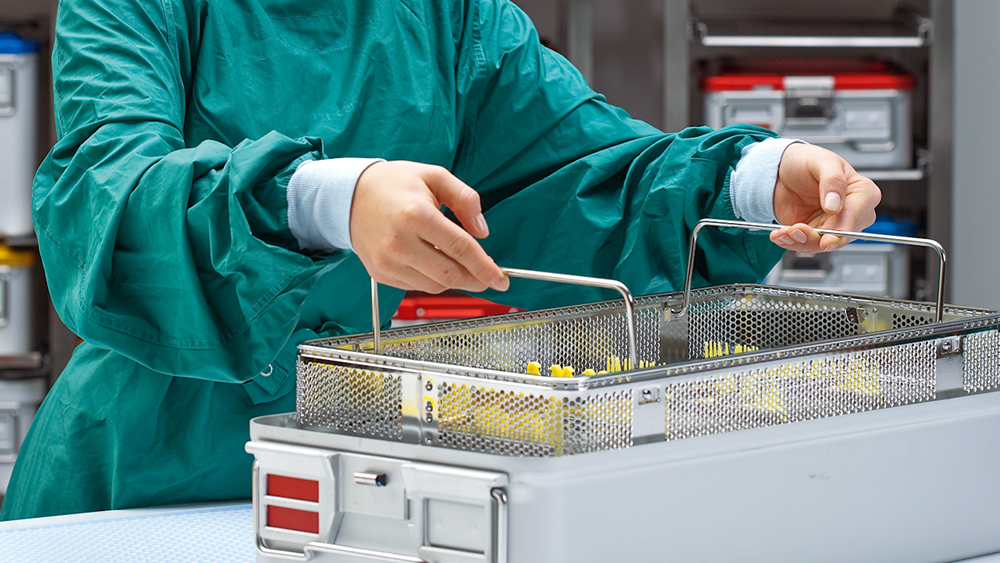 Zaměstnanec oddělení centrální sterilizace zvedá koš s nástroji ze sterilizačního kontejneru