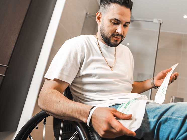 Muž na invalidním vozíku drží v ruce katétr, v pozadí je koupelna